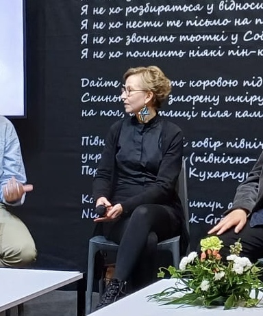 Hanna istuu mustissa vaatteissa, kädessä mikrofoni. Sivuilla näkyy hieman muita ihmisiä. Taustalla on mustavalkoinen koristeteksti. Kirjamessuilla käyneet voivat tulkita, että kuvassa ollaan kirjamessuilla. 