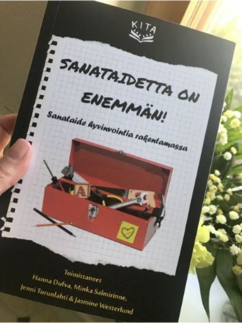 Käsi pitelee kirjaa, jonka kannessa on teksti: Sanataidetta on enemmän! Sanataide hyvinvointia rakentamassa, ja kuva työkalupakista. 