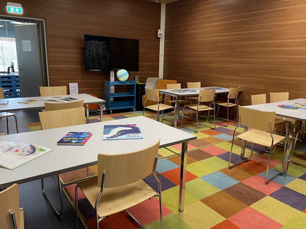 Opetustila, jossa on pienryhmiksi aseteltuja pöytiä ja tuoleja. Huoneessa on värikäs matto ja pöydillä on kirjoja.